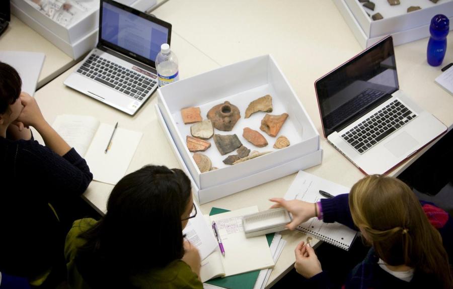 Students working with artifacts on a desk with computers