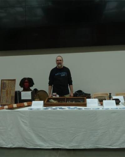 Professor Fred Gleach standing at Anthropology Day event table with display of items from the anthropology collections