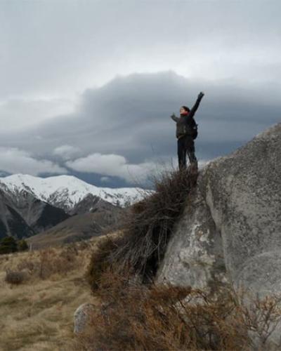 student with arms up in the air on scenic hill